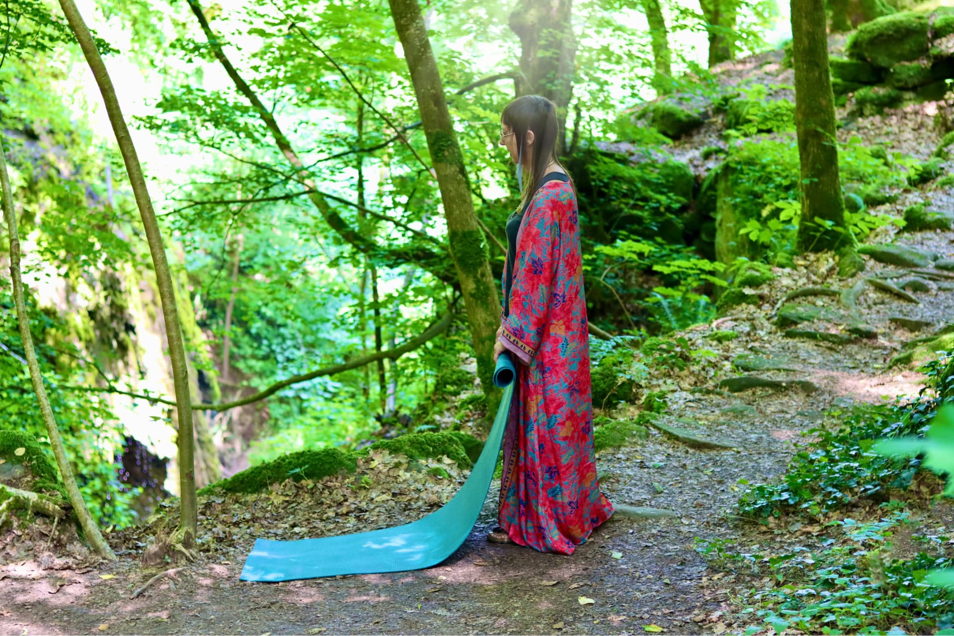 Yogalehrerin mit ausgerollter Yogamatte auf einem Waldweg.