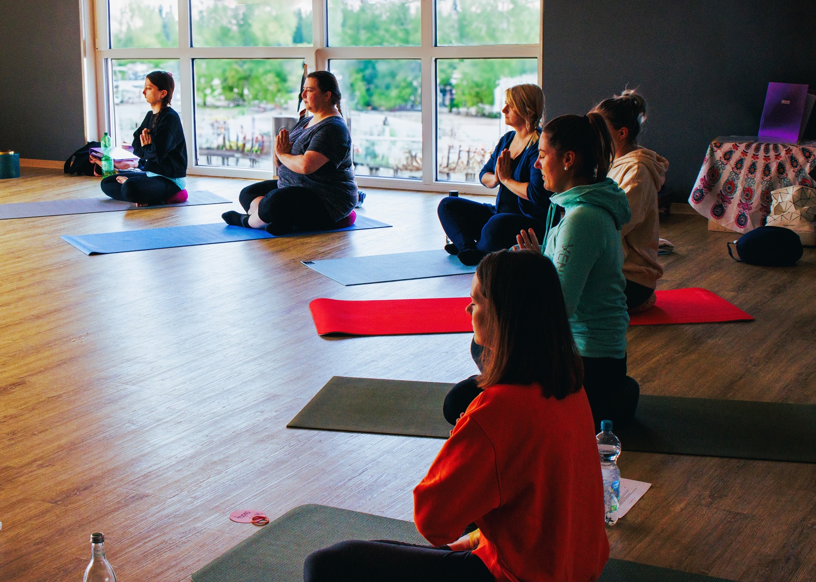 Sechs Teilnehmerinnen sitzen im Namaste während eines Yogaseminars