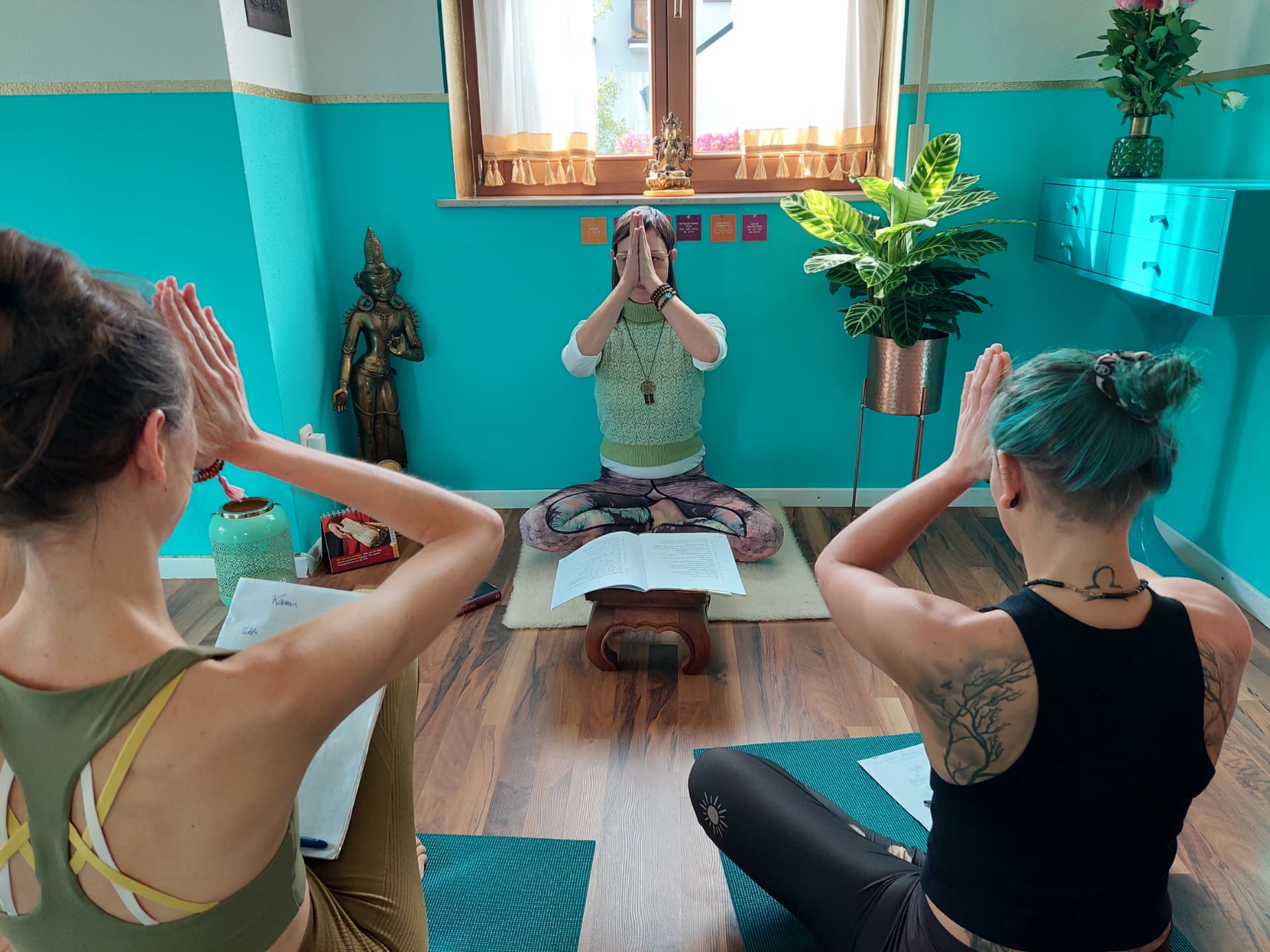 Drei Teilnehmerinnen üben gemeinsam Namaste im Kursraum