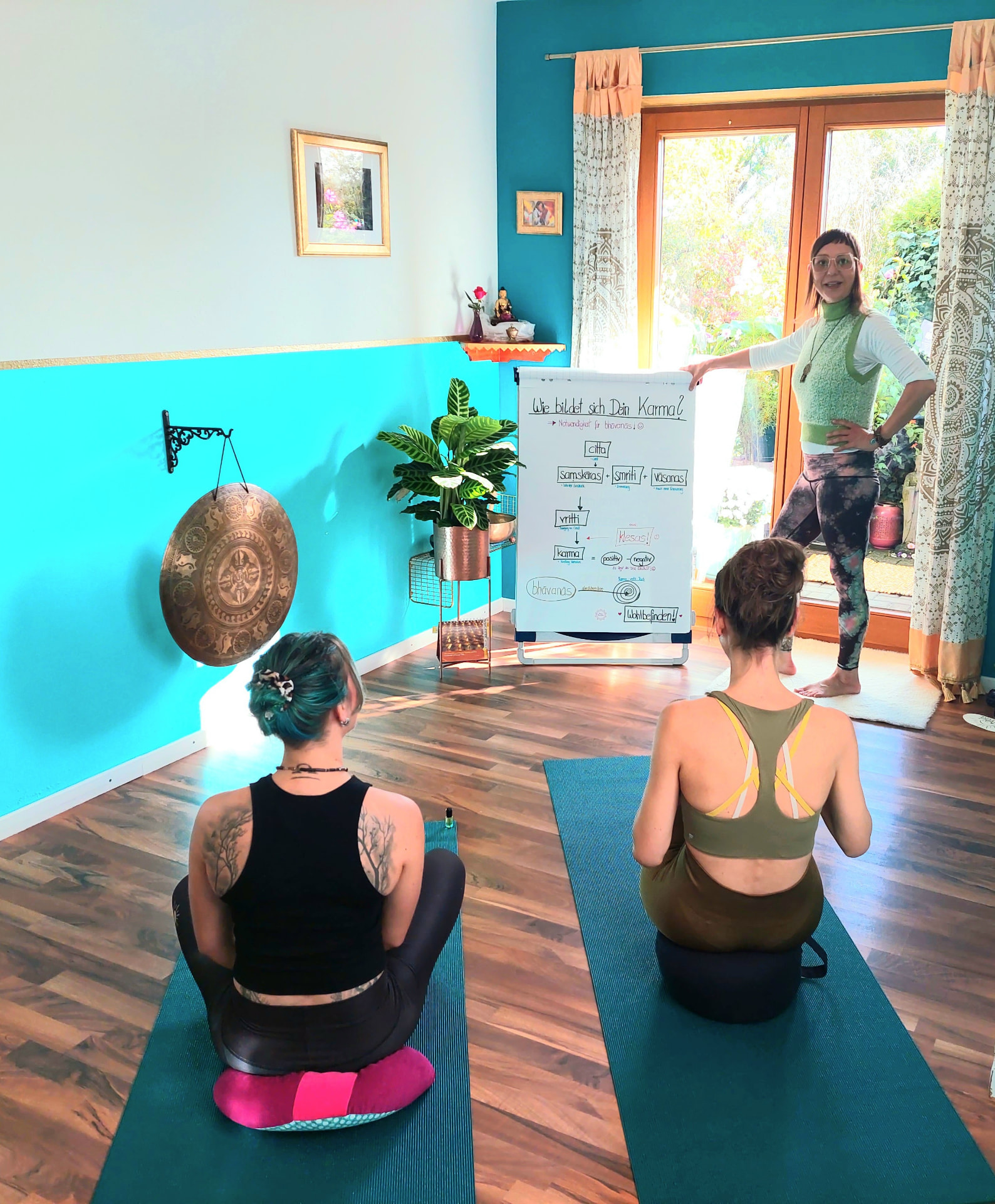 Nadine erklärt zwei Teilnehmerinnen im Yogaraum die Zusammenhänge von Karma und Wohlbefinden.