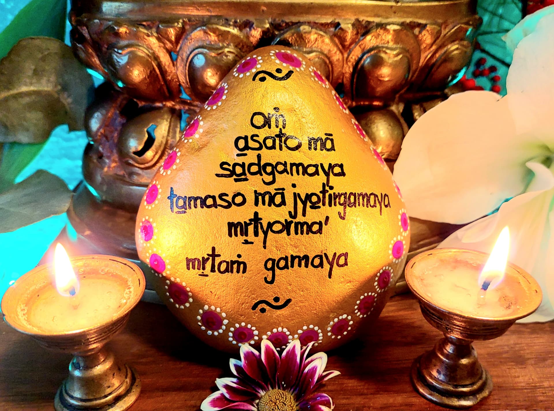 Goldener Stein mit dem Mantra asato mā sadgamaya zwischen zwei Kerzen.